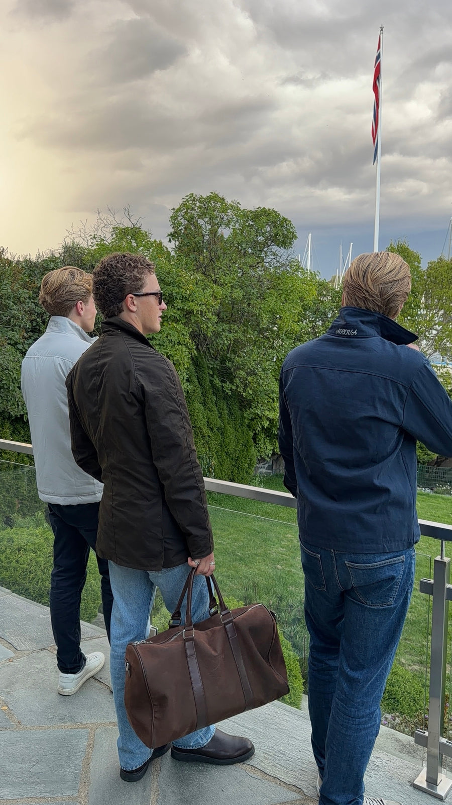 Tre venner ved sjøen, én i Navy Overshirt med ASCOVA på kragen, én med Suede Duffel